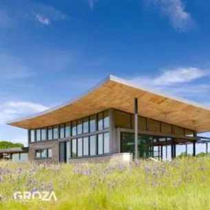 House with a broad, sweeping timber roof above a spring meadow