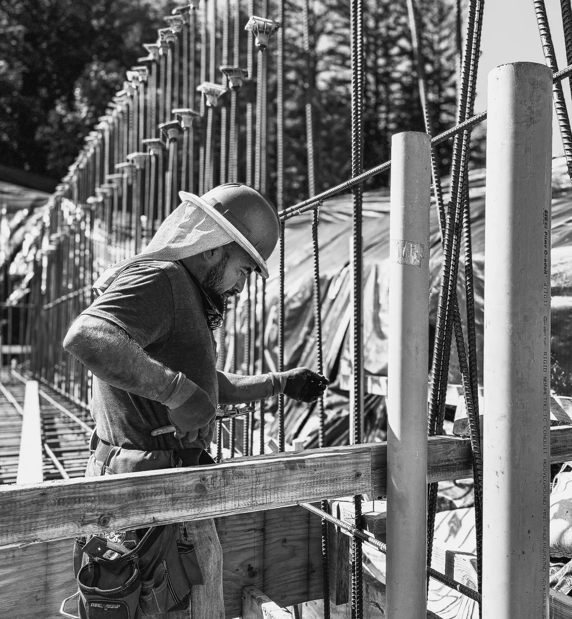 Black-and-white photo of a builder working at concrete formwork and rebar