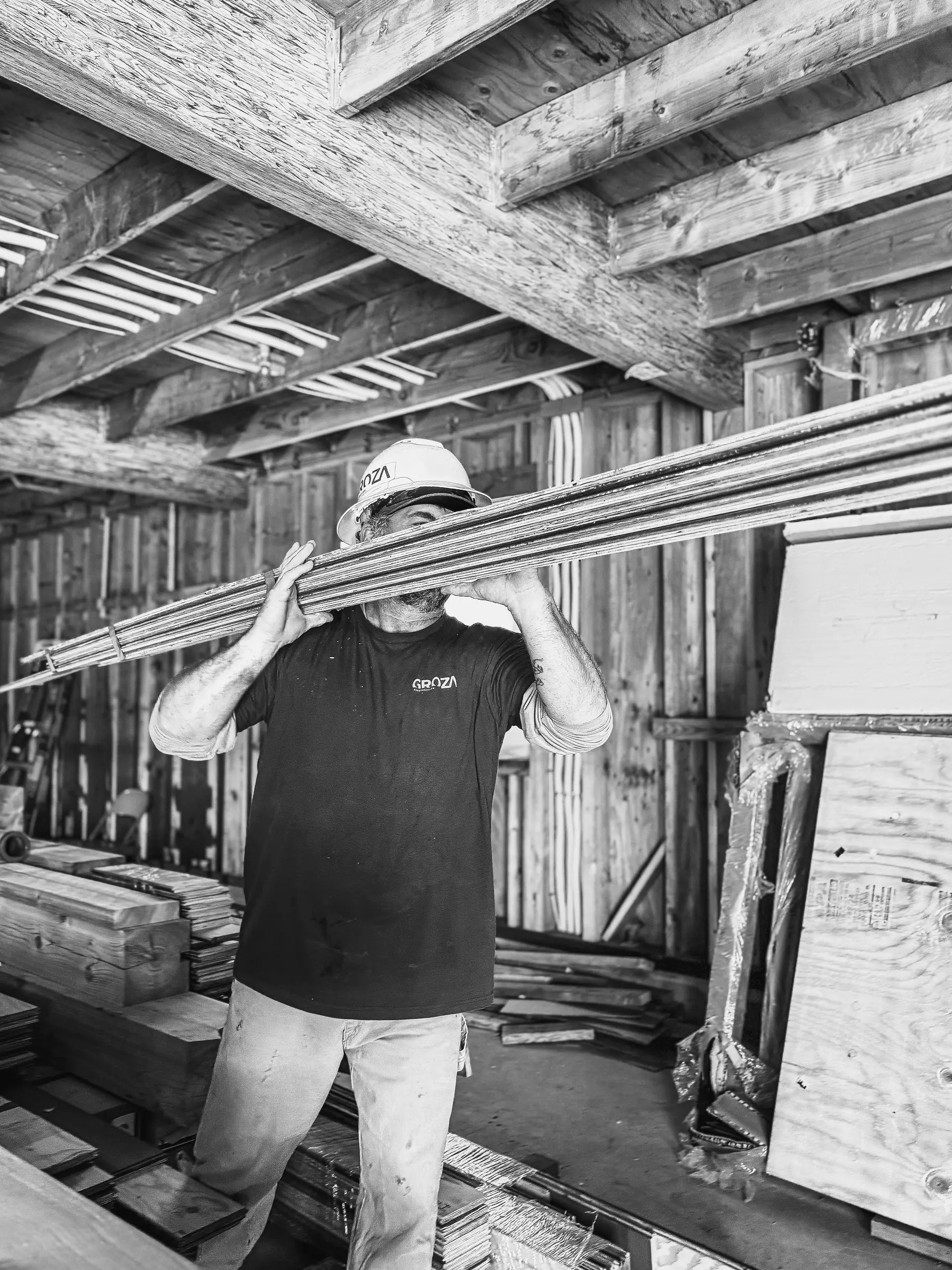 Black-and-white photo of a Groza carpenter carrying lumber through a framed structure
