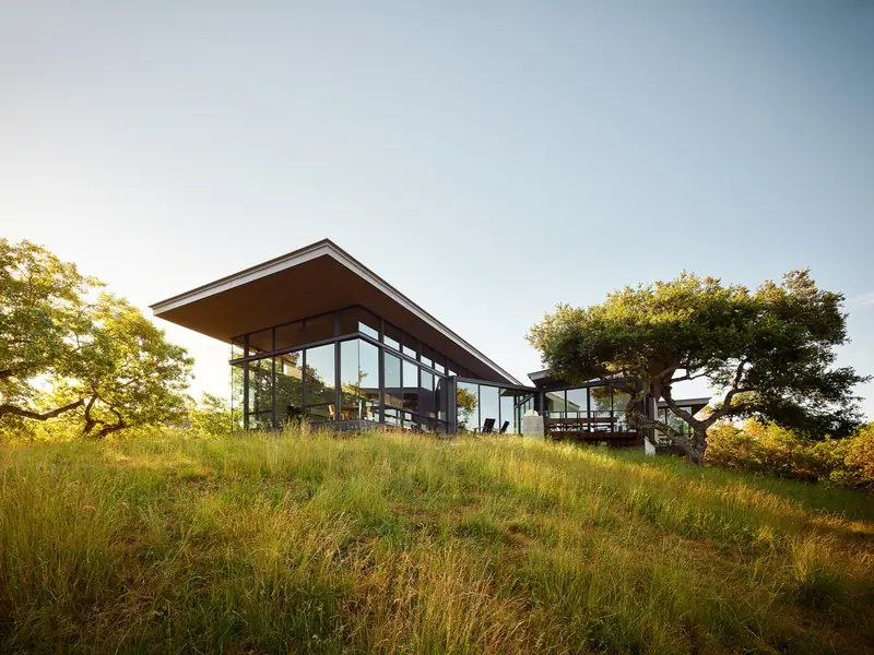 Low glass pavilion with a floating angled roof set in a golden hillside meadow