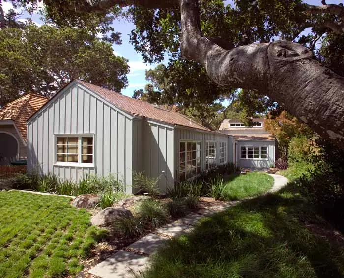 Gray board-and-batten cottage with a garden path under a spreading oak