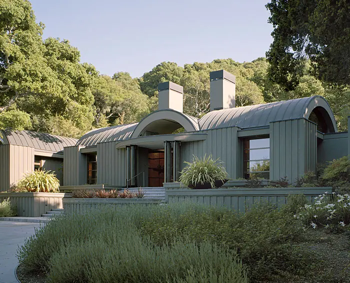 Sage-green standing-seam roofs curving over a long, low house ringed by lavender