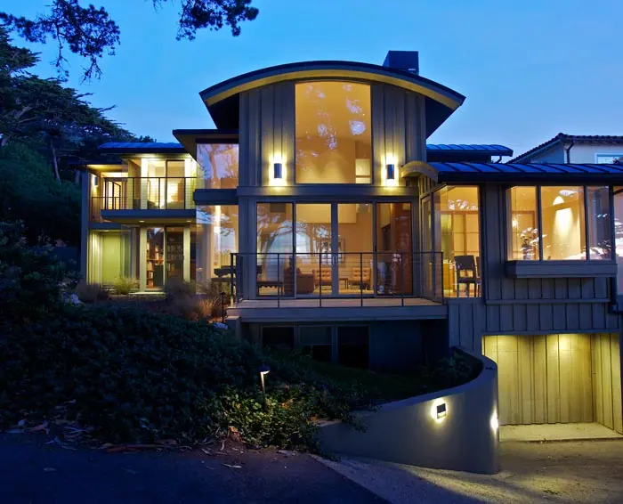 Multi-story residence glowing at dusk with a wall of windows above the garage