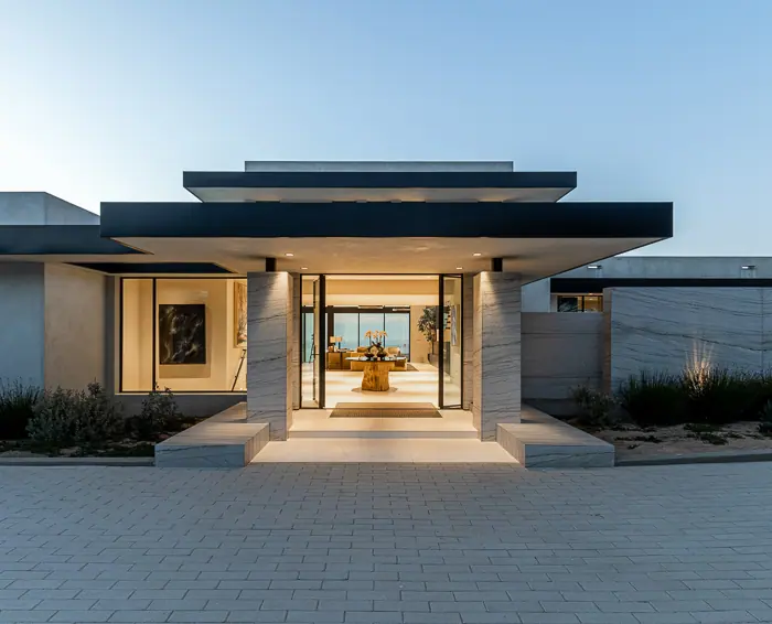 Flat-roofed modern entry pavilion glowing against an evening sky