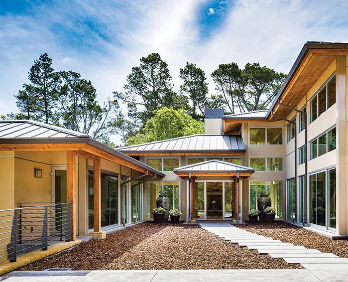 Courtyard entry of a two-story timber and glass house with a standing-seam metal roof