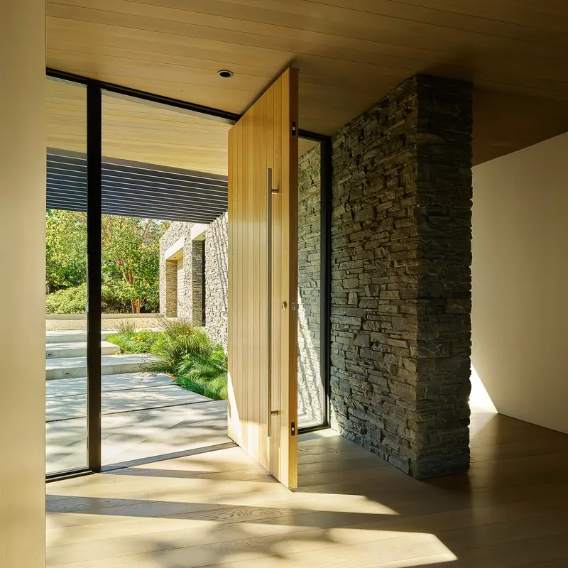 Oversized timber pivot door beside a dry-stacked stone wall