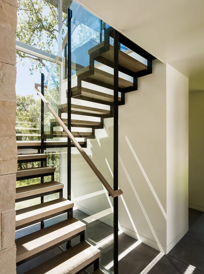 Open-riser steel and oak stair rising through a glass-walled stairwell