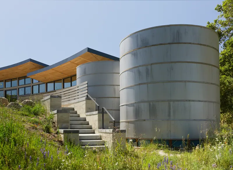 Two weathered steel water tanks beside a stepped path and a low wood-roofed house