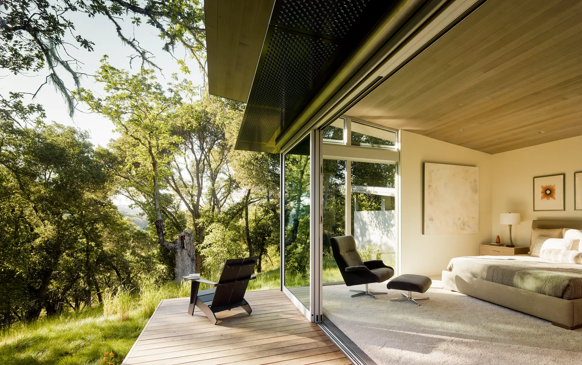 Primary suite opening through sliding glass walls to a canopy of coast live oaks