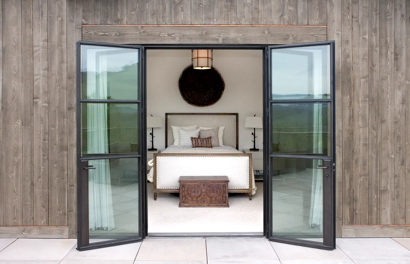 Bedroom seen through steel French doors set in a weathered wood wall