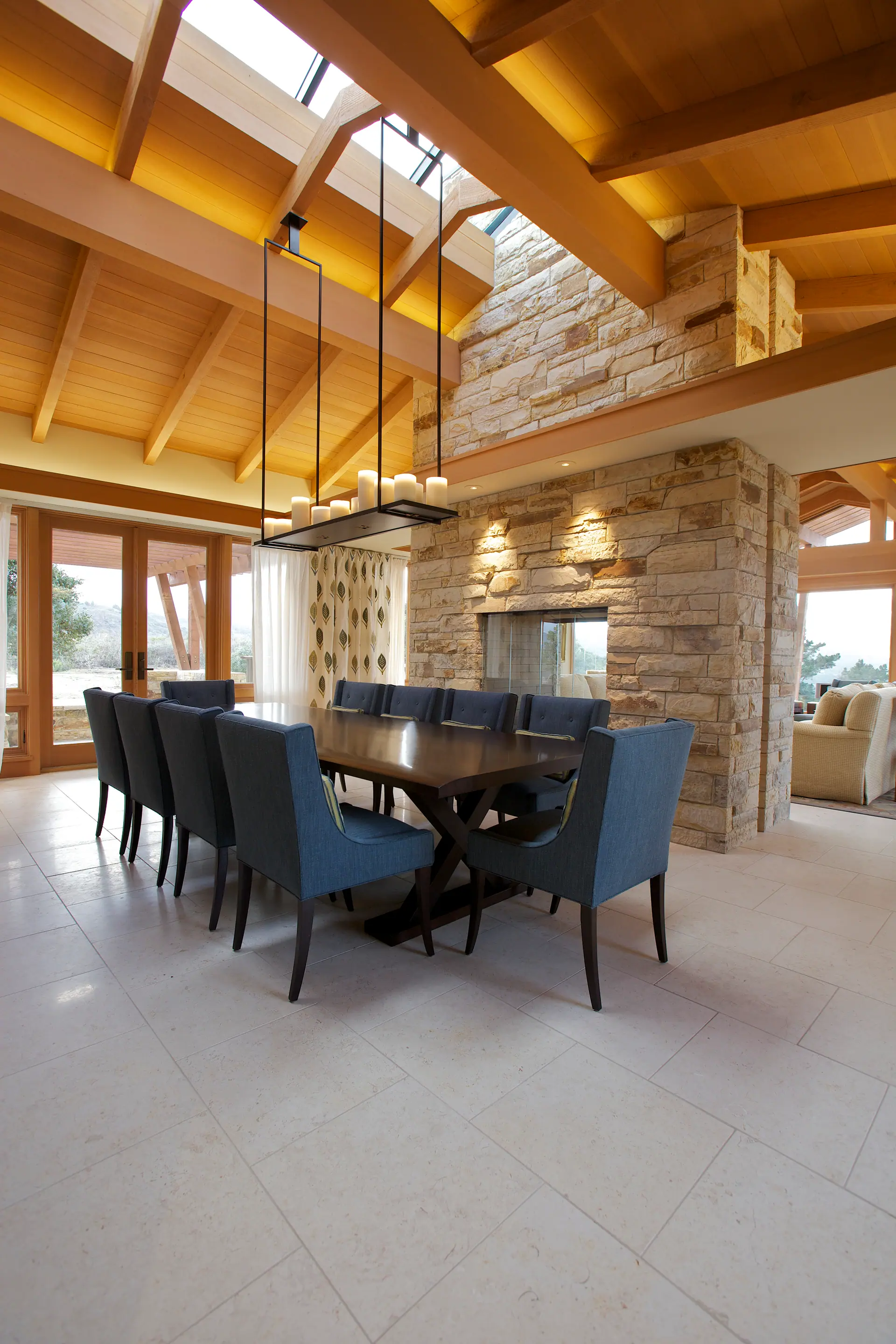 Dining room with a long table, blue chairs and a stone fireplace beneath a vaulted timber ceiling