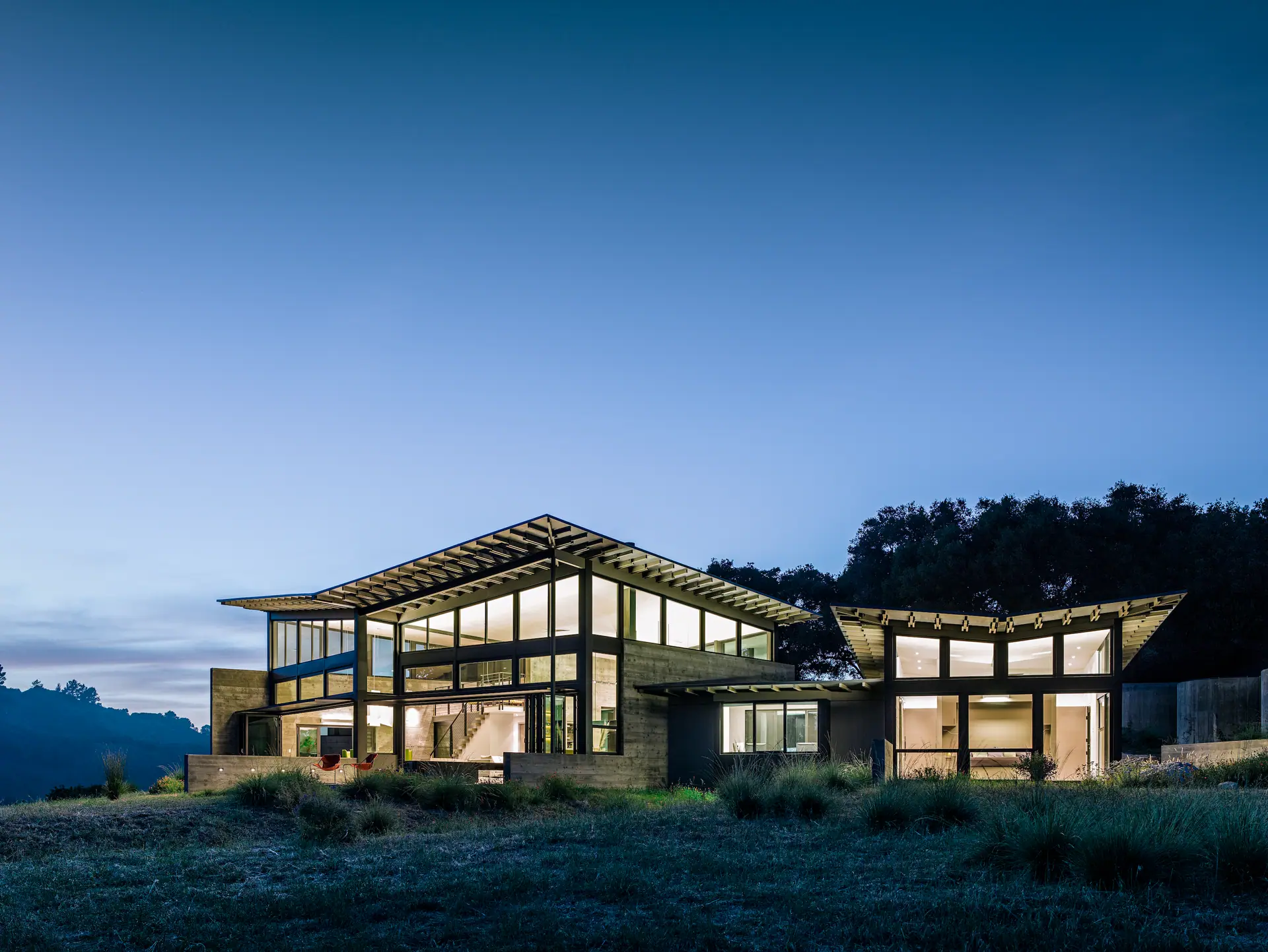 Steel-framed house with a floating roof glowing against a deep blue evening sky